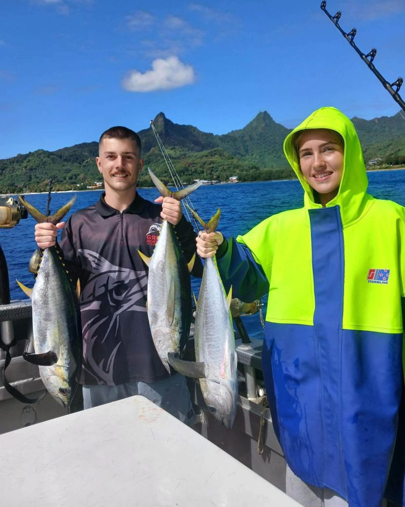 A pair holding yellowfin tuna with the island behind