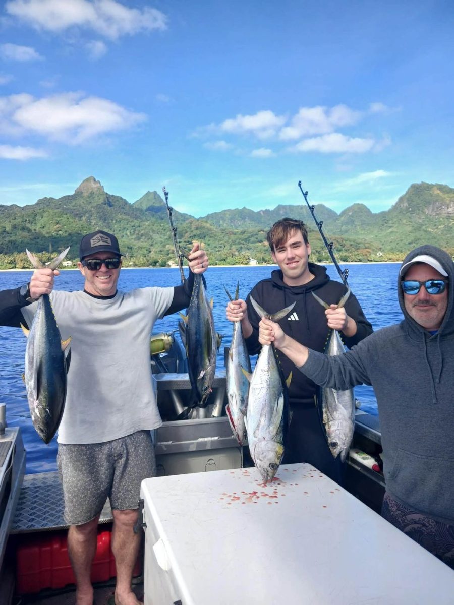 Three anglers holding yellowfin tuna in front of the mountains